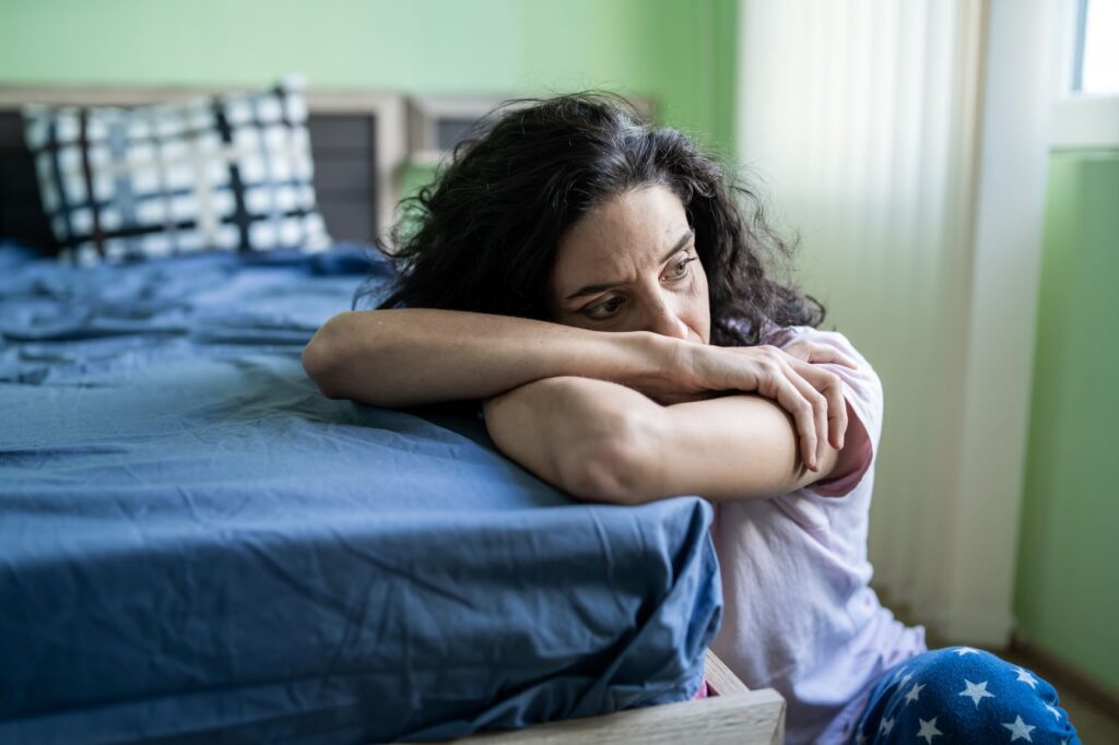 woman feeling tired sitting on the floor resting her head on the bed